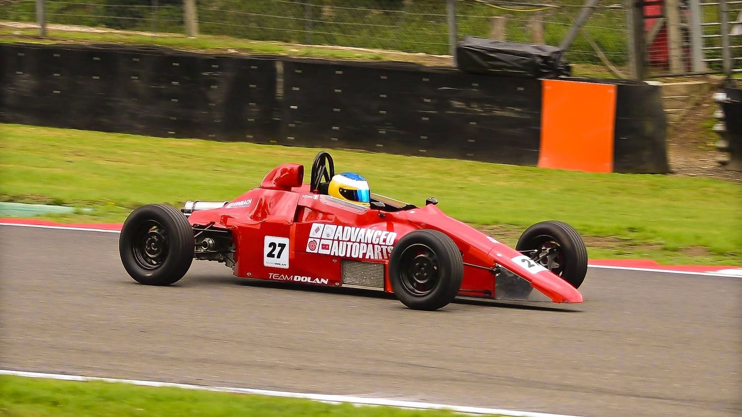 Red single-seater race car cornering past a track marker, motorsport photography
