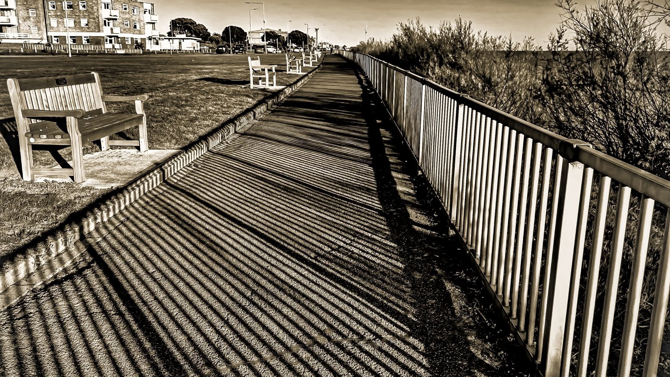Sepia-toned seafront promenade with benches and a striped railing, coastal landscape photography