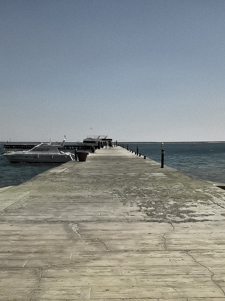 Wooden jetty leading out to moored boats on calm water, coastal landscape photography