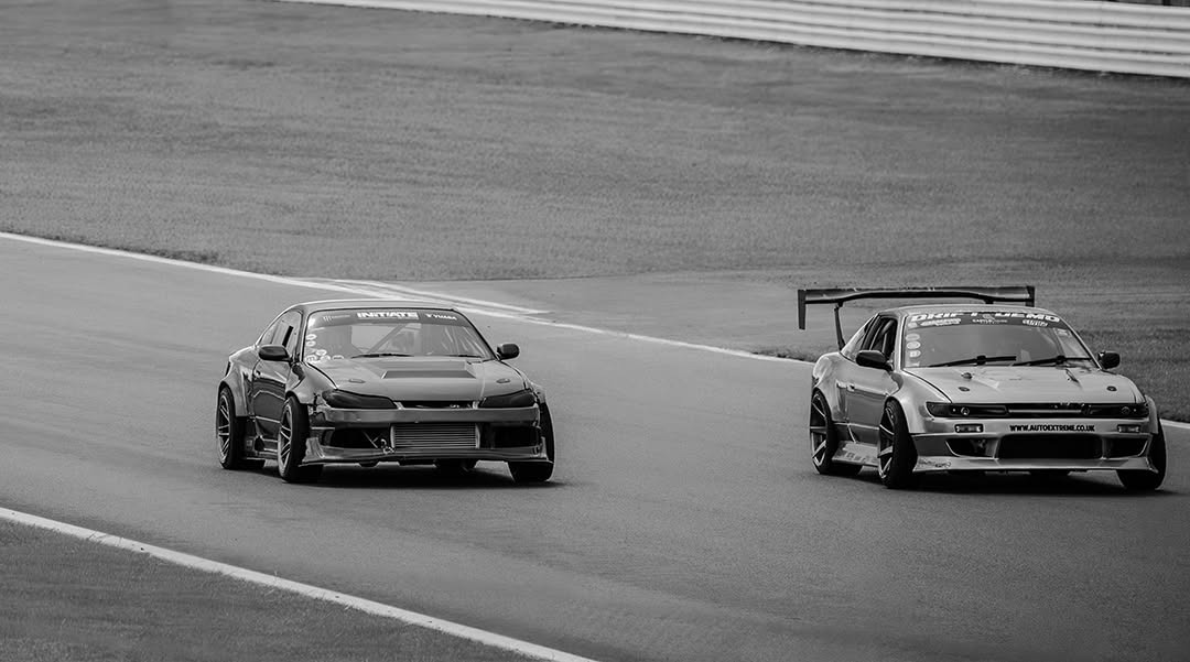 Two drift cars cornering together on a race track, black and white motorsport photography