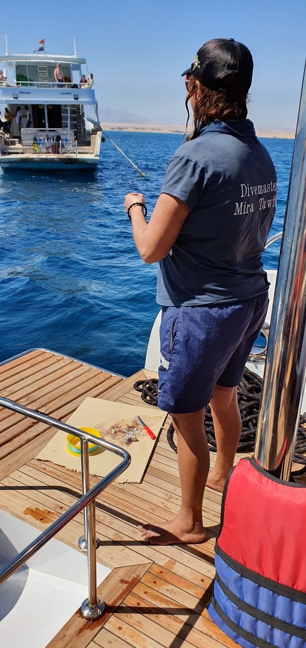 Crew member on a dive boat deck with the sea and a moored boat behind, travel landscape photography