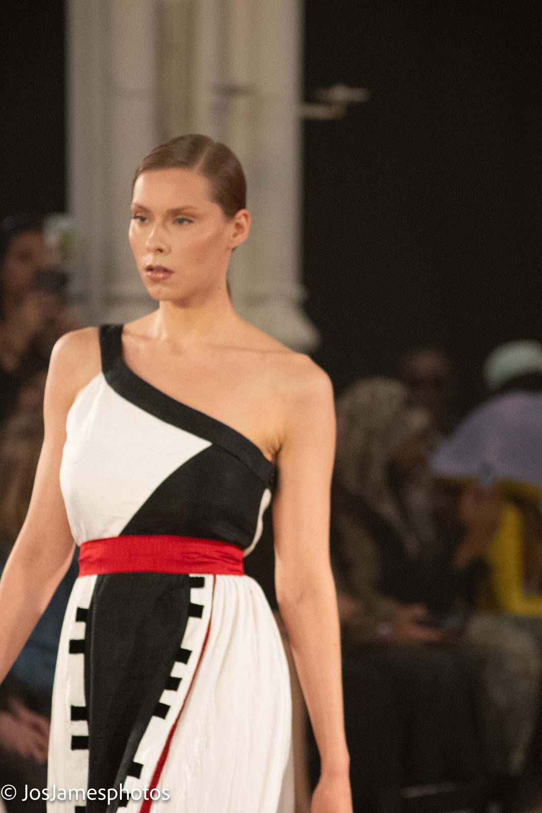 Model in a black and white asymmetric dress with red sash on the catwalk, London Fashion Week 2026