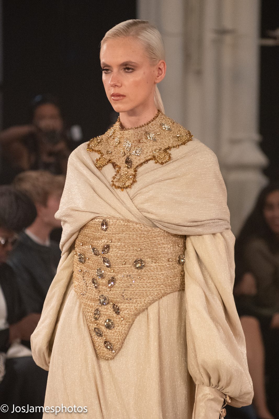 Model in a cream draped cape with gold embroidery on the catwalk, London Fashion Week 2026 event photography