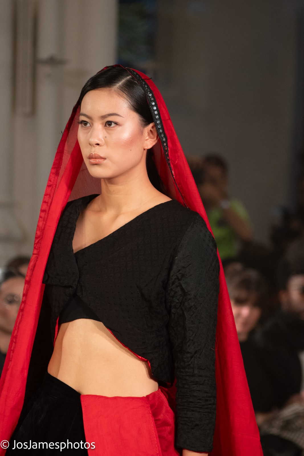 Model in a red hooded cape and black top on the catwalk, London Fashion Week 2026