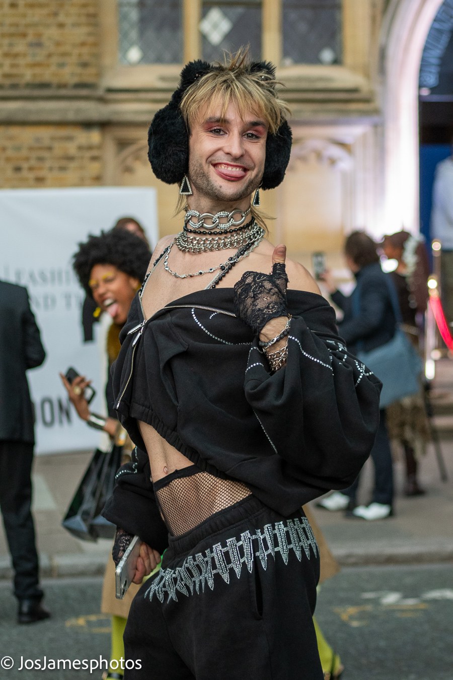 Guest in faux-fur earmuffs, lace gloves and chains giving a thumbs up outside the show, London Fashion Week 2026 event photography